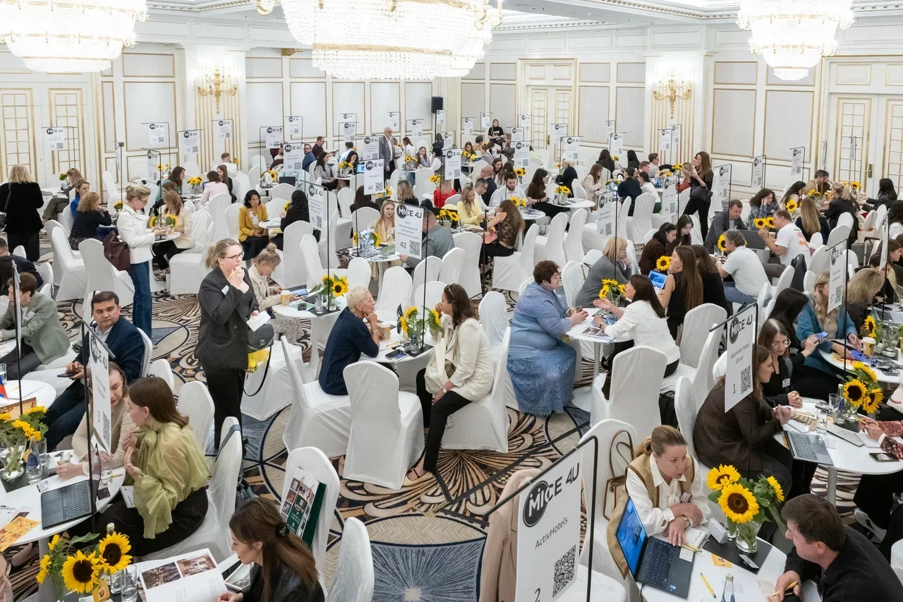 The MICE4U workshop floor: dozens of round tables with exhibitor signs and sunflowers